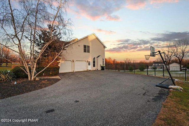 property exterior at dusk featuring a garage, driveway, and fence