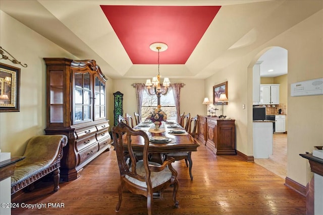 dining room featuring arched walkways, a tray ceiling, wood finished floors, a chandelier, and baseboards