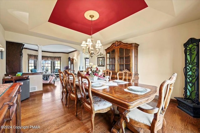 dining room featuring arched walkways, a raised ceiling, visible vents, wood finished floors, and ornate columns