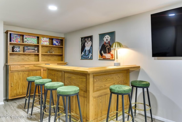 bar with baseboards, a bar, and light wood-style floors