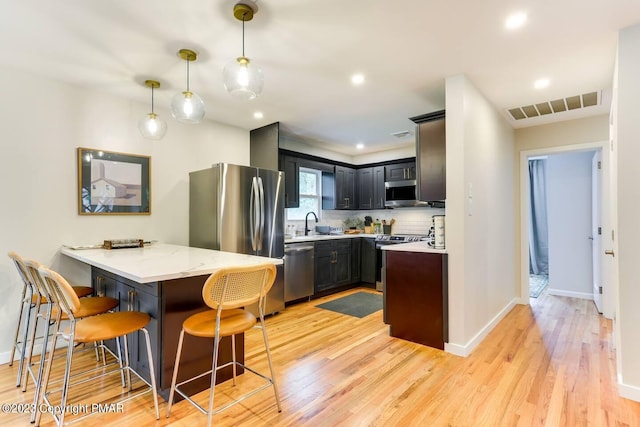 kitchen featuring visible vents, a breakfast bar, a peninsula, stainless steel appliances, and light wood-style floors