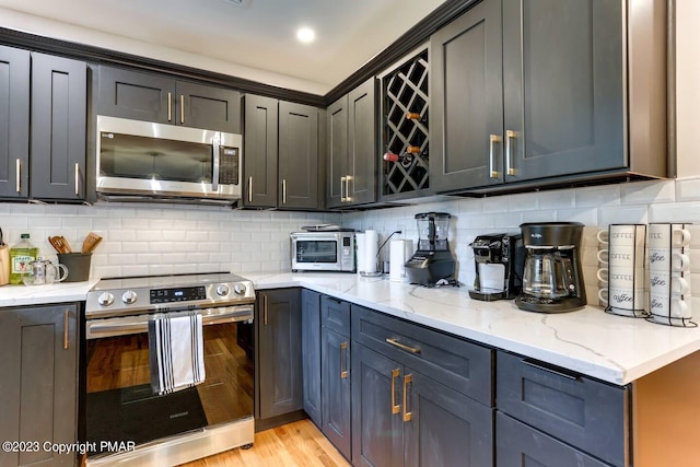 kitchen featuring appliances with stainless steel finishes, decorative backsplash, light wood finished floors, and light stone countertops