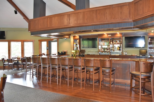 bar with high vaulted ceiling, wet bar, and wood finished floors