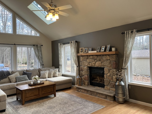 living room featuring a wealth of natural light, a stone fireplace, baseboards, and wood finished floors