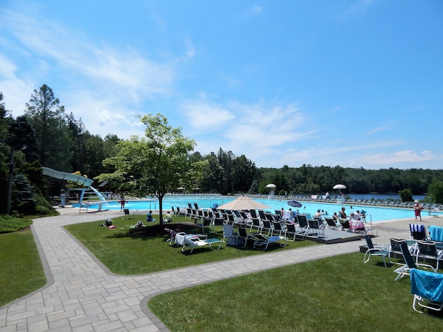 view of property's community with a wooded view, a lawn, a water view, and a swimming pool