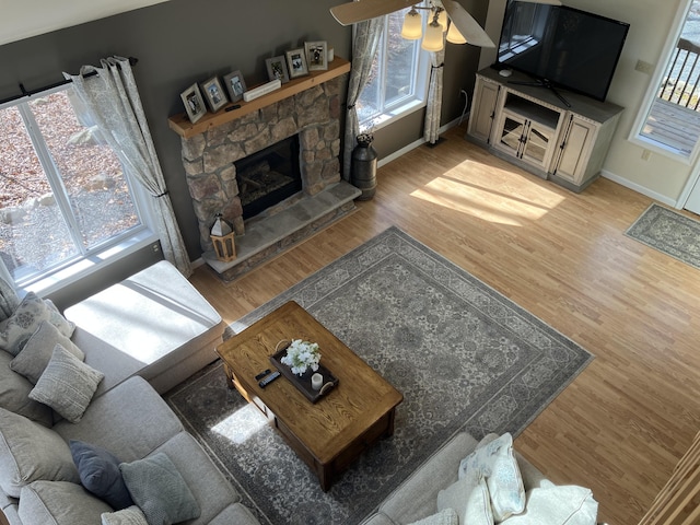 living area featuring a healthy amount of sunlight, a fireplace, baseboards, and wood finished floors