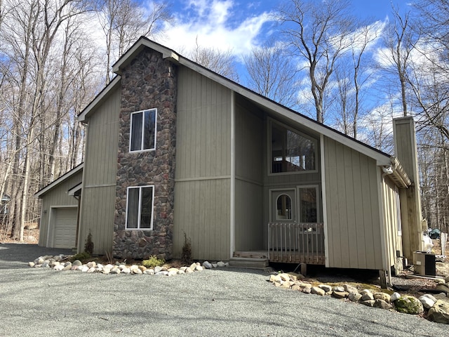 view of front of property featuring aphalt driveway, a chimney, central air condition unit, an attached garage, and stone siding