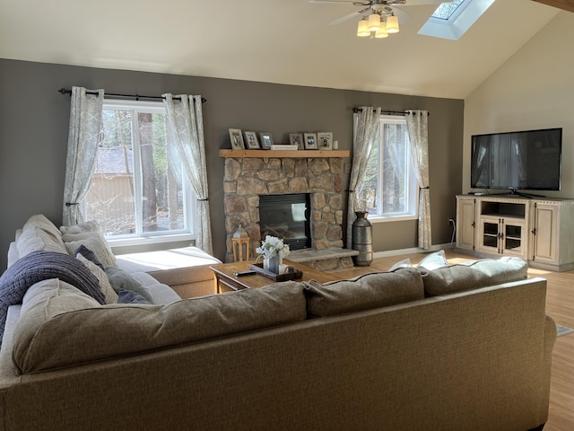 living room with light wood-type flooring, vaulted ceiling with skylight, a fireplace, and a healthy amount of sunlight