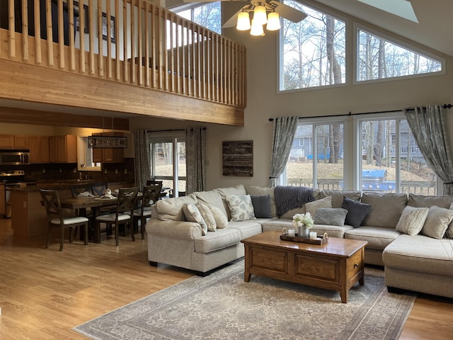 living room with a ceiling fan, a high ceiling, and light wood finished floors