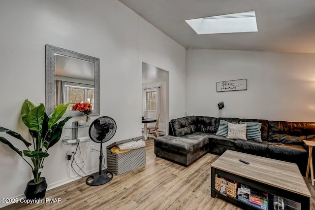 living room featuring lofted ceiling with skylight and light hardwood / wood-style flooring