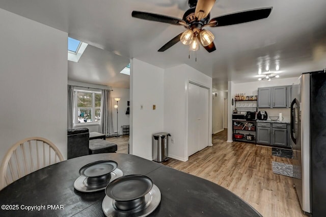 dining space featuring ceiling fan, light wood-type flooring, and a skylight