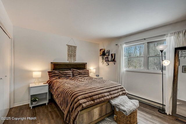 bedroom with baseboard heating, hardwood / wood-style floors, and a closet