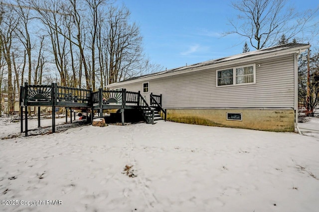 snow covered back of property with a wooden deck