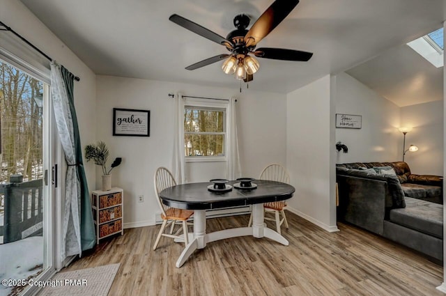 dining room with ceiling fan, light wood-type flooring, and a skylight