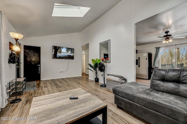 living room with ceiling fan, vaulted ceiling with skylight, and hardwood / wood-style floors