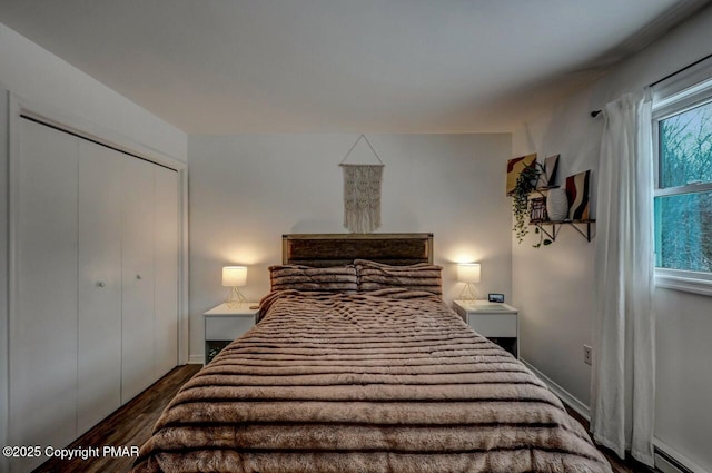 bedroom with baseboard heating, dark hardwood / wood-style floors, and a closet