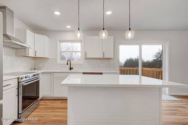 kitchen with light wood-type flooring, light countertops, electric range, and wall chimney exhaust hood