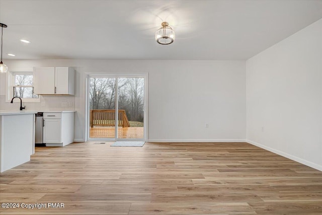 unfurnished dining area with light wood-style floors, recessed lighting, a sink, and baseboards