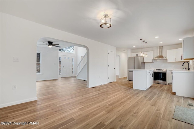 kitchen with arched walkways, a kitchen island, appliances with stainless steel finishes, open floor plan, and wall chimney range hood