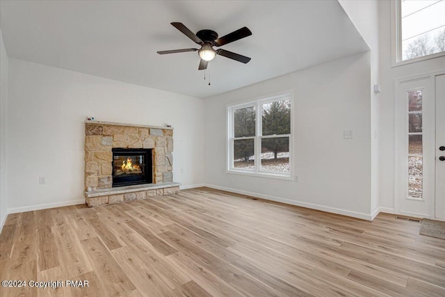 unfurnished living room featuring a stone fireplace, a ceiling fan, light wood-style flooring, and baseboards