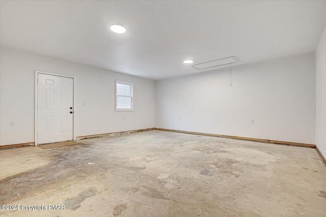 unfurnished room featuring concrete flooring, attic access, and baseboards