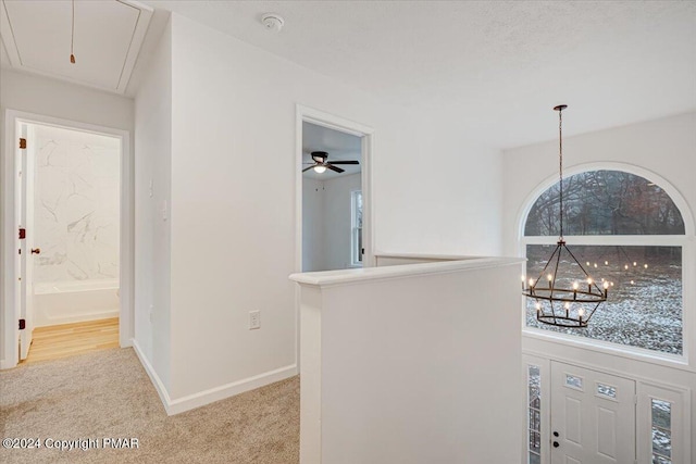 hallway featuring a chandelier, light carpet, an upstairs landing, baseboards, and attic access