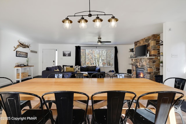 dining space with a stone fireplace and ceiling fan