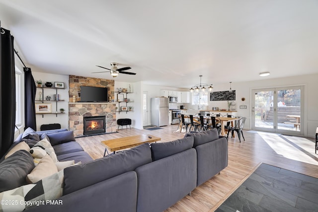 living room with a stone fireplace, ceiling fan with notable chandelier, and light wood-type flooring