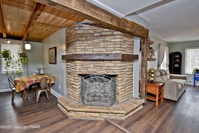 living area with vaulted ceiling with beams, wood ceiling, a stone fireplace, wood finished floors, and baseboards