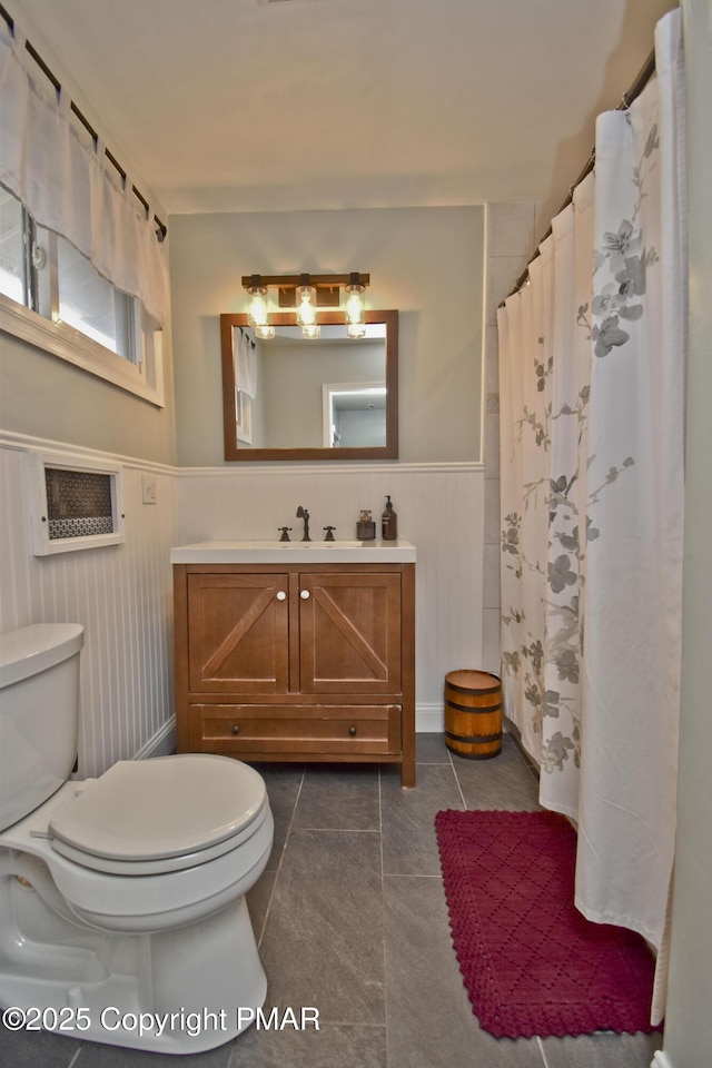 full bathroom with tile patterned flooring, wainscoting, vanity, and toilet