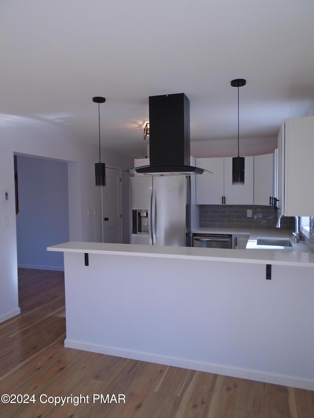 kitchen featuring island range hood, a peninsula, wood finished floors, stainless steel appliances, and a sink