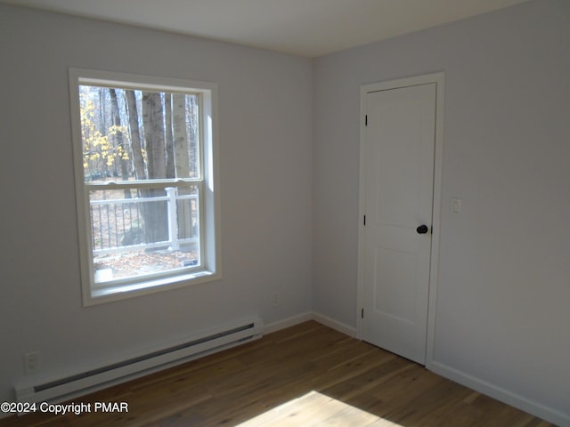 empty room with wood finished floors, baseboards, and baseboard heating