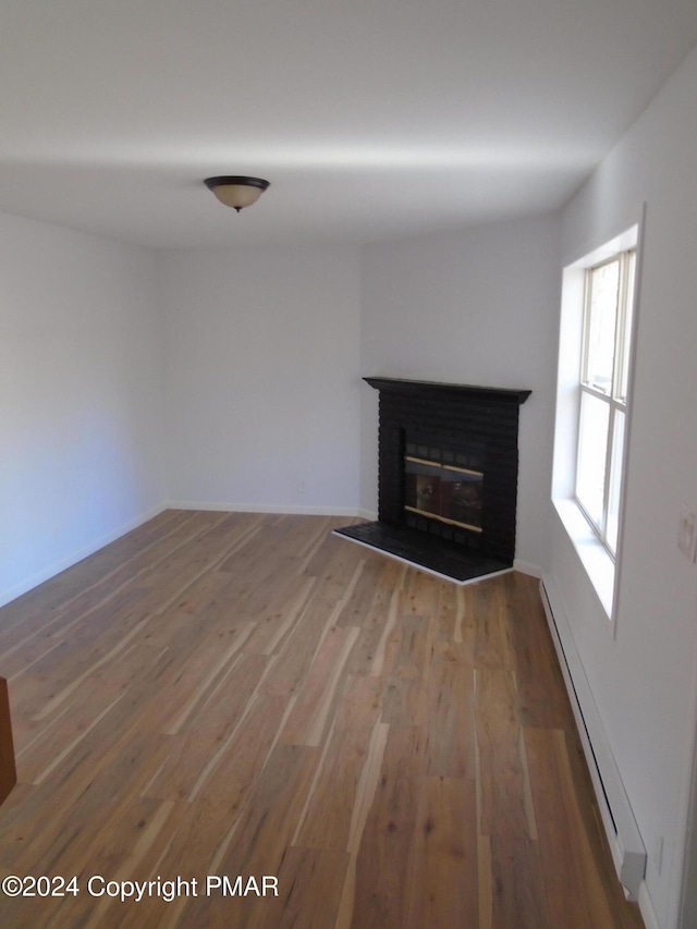 unfurnished living room featuring a brick fireplace, wood finished floors, and a baseboard radiator