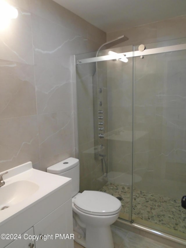 full bathroom with vanity, tile walls, toilet, and a stall shower