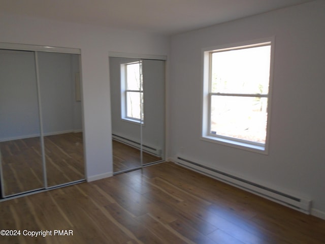 unfurnished bedroom with a baseboard heating unit, multiple closets, and wood finished floors