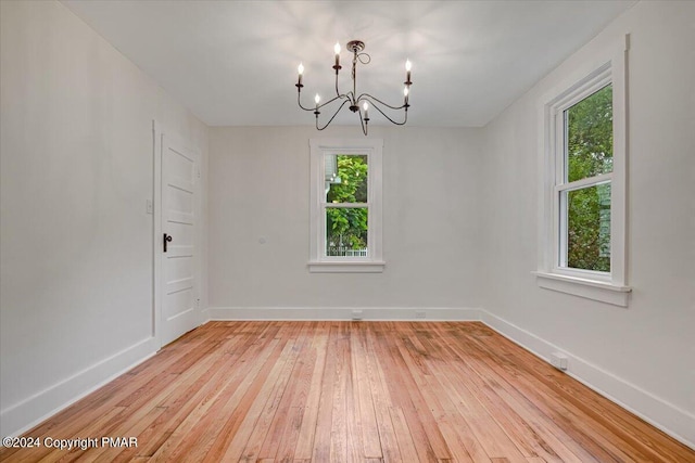 empty room featuring light wood-style floors, baseboards, and a notable chandelier