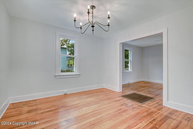 empty room featuring baseboards, light wood finished floors, a wealth of natural light, and an inviting chandelier