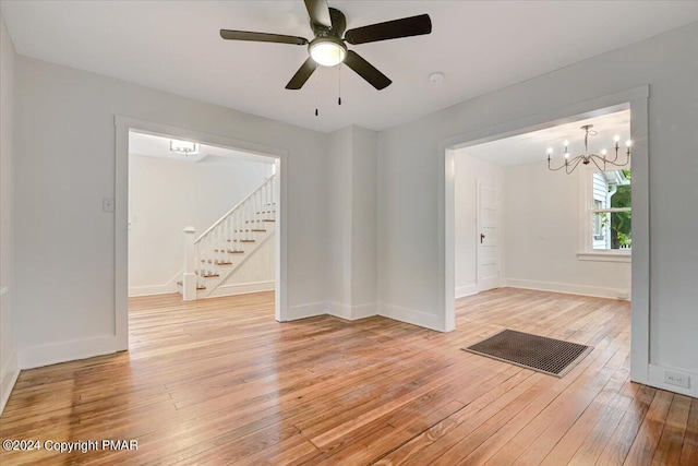 spare room featuring baseboards, stairway, light wood finished floors, and ceiling fan with notable chandelier