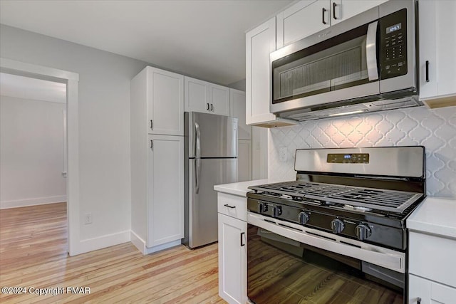 kitchen featuring white cabinets, decorative backsplash, appliances with stainless steel finishes, light countertops, and light wood-type flooring