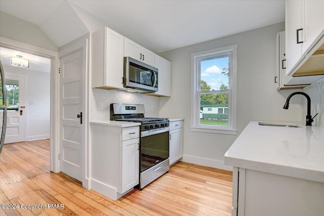 kitchen featuring tasteful backsplash, light wood-style flooring, appliances with stainless steel finishes, white cabinetry, and a sink