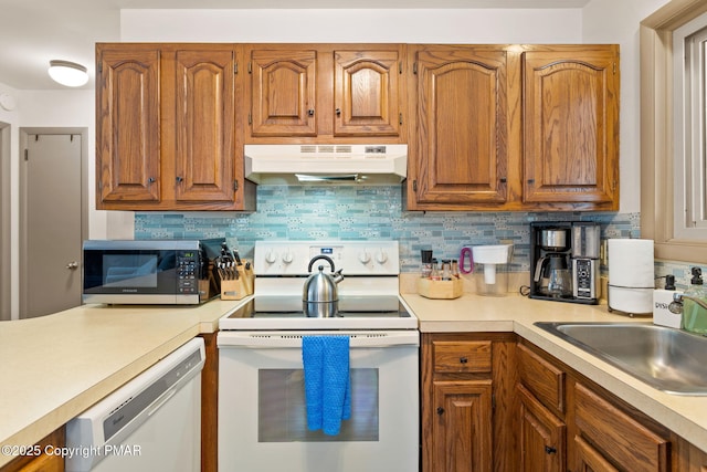 kitchen with under cabinet range hood, white appliances, a sink, light countertops, and decorative backsplash