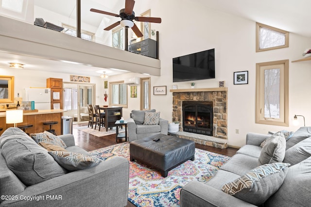 living area with ceiling fan, high vaulted ceiling, a stone fireplace, wood finished floors, and a wall mounted air conditioner