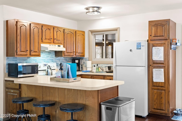 kitchen with white appliances, a breakfast bar, a peninsula, light countertops, and under cabinet range hood