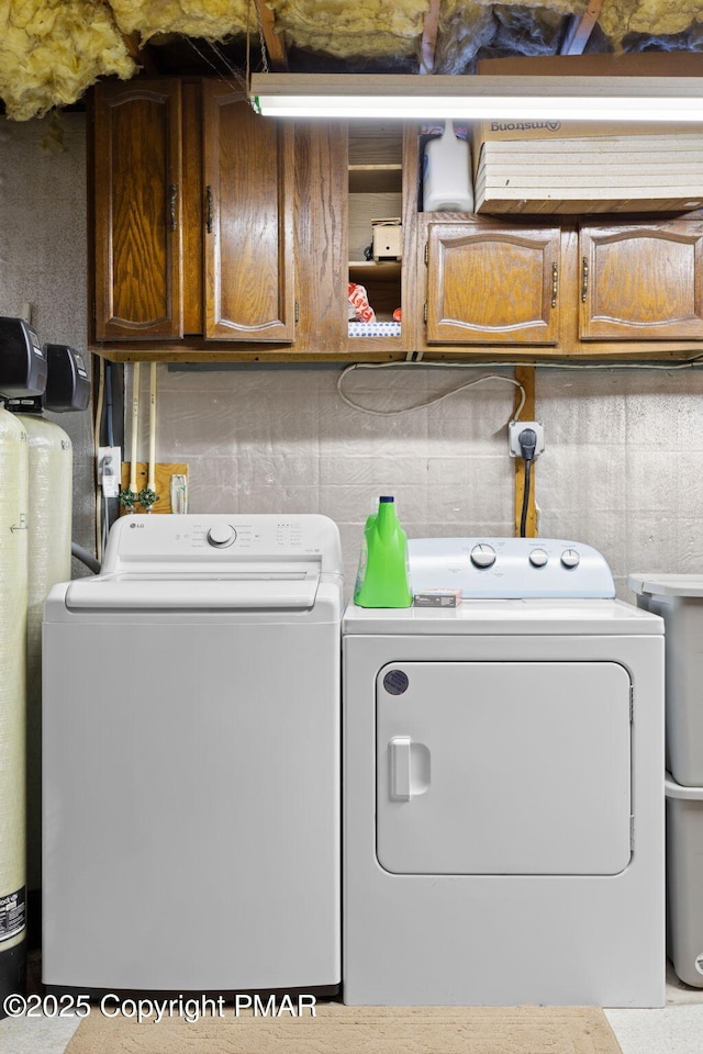 clothes washing area with separate washer and dryer and cabinet space