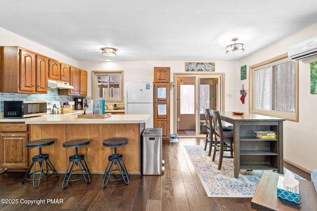 kitchen featuring under cabinet range hood, a peninsula, range, freestanding refrigerator, and stainless steel microwave