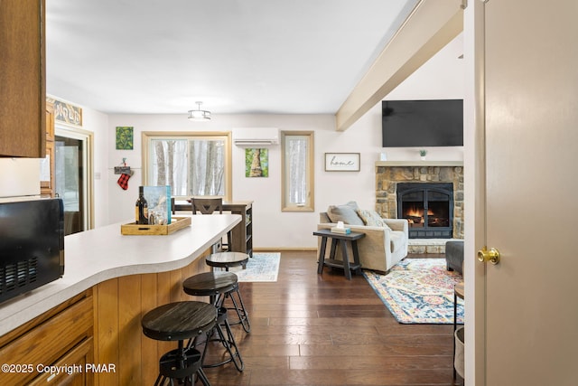 kitchen with a wall unit AC, dark wood-style flooring, light countertops, a kitchen bar, and black microwave