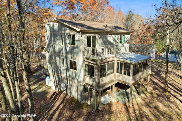 rear view of property featuring a sunroom, roof with shingles, and a balcony