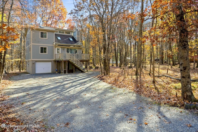 view of front of home with gravel driveway, an attached garage, stairs, and a shingled roof