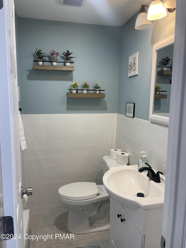 half bath with vanity, tile patterned floors, toilet, and tile walls