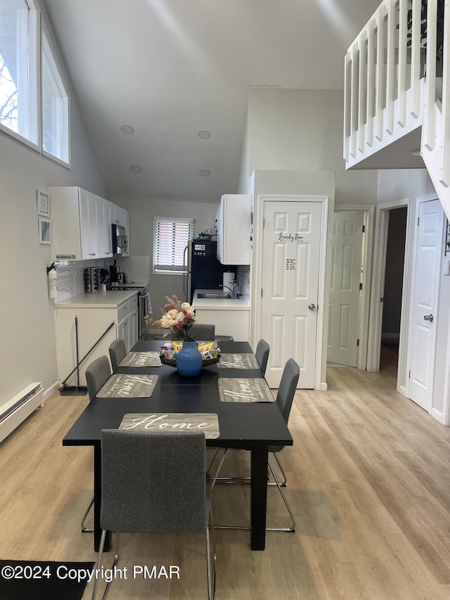 dining space featuring baseboard heating, light wood-style flooring, and a towering ceiling